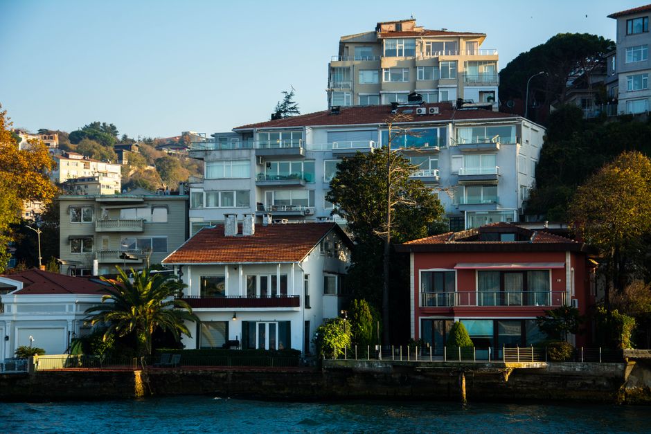 A view of several multi-storey residential buildings situated on a hillside in Richmond upon Thames, with some houses featuring large glass windows, balconies, and rooftop terraces. The lower part of